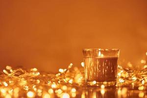 Burning candle with a golden garland lights in bokeh on dark background photo