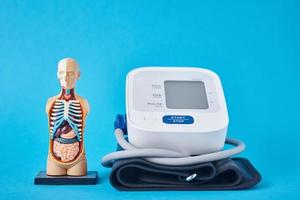 monitor de presión arterial digital y modelo humano anatómico sobre un fondo azul, primer plano. concepto de salud y medicina foto