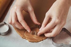 Making gingerbread cookies in the shape of a heart for Valentines Day. Woman hand use cookie cutter. Holiday food concept photo