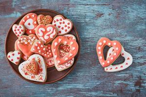 Decorated heart shape cookies in white plate and two cookies on the gray background, top view. Valentines Day food concept photo