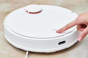 Hand push start button on robot vacuum cleaner. Modern smart household