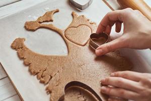 Making gingerbread cookies in the shape of a heart for Valentines Day. Woman hand use cookie cutter. Holiday food concept photo