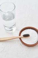 Bamboo toothbrush, baking soda and glass of water on white background photo