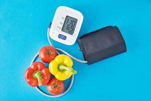 Digital blood pressure monitor and fresh vegetables on a blue background. Healthcare concept photo