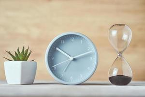 Hourglass, alarm clock and plant on the table, close up photo