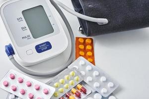 Digital blood pressure monitor and medical pills on the white table. Healthcare and medicine concept photo