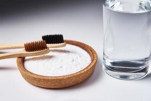 Bamboo toothbrushes, baking soda and glass of water on white background photo