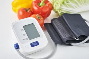 monitor de presión arterial digital y verduras frescas en la mesa. concepto de salud foto