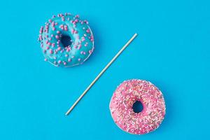 dos donuts separados con una pajita sobre fondo azul. concepto de comida creativa foto