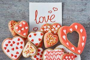 Decorated and glazed heart shape cookies and paper note with inscription LOVE on the gray background, top view. Valentines day concept photo