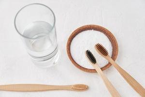 Bamboo toothbrushes, baking soda and glass of water on white background photo