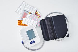 Digital blood pressure monitor and medical pills on the white table. Healthcare and medicine concept photo