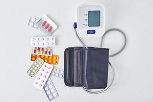 monitor de presión arterial digital y pastillas médicas en la mesa blanca. concepto de salud y medicina foto
