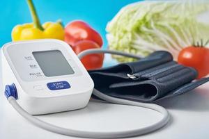 monitor de presión arterial digital y verduras frescas en la mesa con fondo azul. concepto de salud foto
