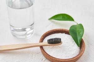 Bamboo toothbrush, baking soda and glass of water on white background photo