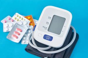 Digital blood pressure monitor and medical pills on a blue background. Healthcare and medicine concept photo