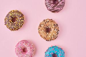 Different types of a colorful donats decorated sprinkles and icing on pastel pink background photo