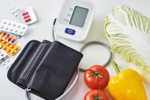 Digital blood pressure monitor, fresh vegetables and medical pills on a white background. Healthy lifestyle concept photo