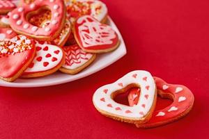 Decorated heart shape cookies in white plate and two cookies on the red background. Valentines Day food concept photo