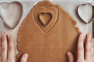 Making gingerbread cookies in the shape of a heart for Valentines Day. Woman hand use cookie cutter. Holiday food concept photo