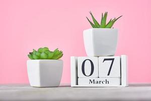 Wooden block calendar with date 7 march and plant on the pink background photo