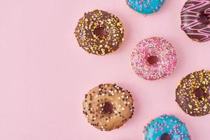 Pattern with different types of colorful donats decorated sprinkles and icing on a pastel pink background, top view flat lay photo