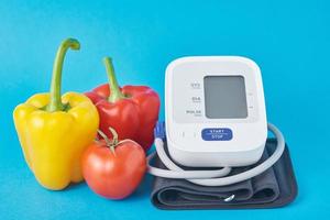 Digital blood pressure monitor and fresh vegetables on a blue background. Healthcare concept photo