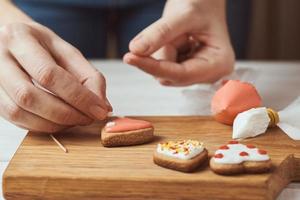 Decorating gingerbread cookies with icing. Woman hand decorate cookies in shape of heart, closeup photo