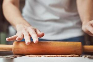 manos femeninas rodando masa sobre la mesa, primer plano. mujer haciendo masa para hornear en la cocina foto