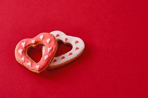 Two decorated with icing and glazed heart shape cookies on the red background with copy space. Valentines Day food concept photo