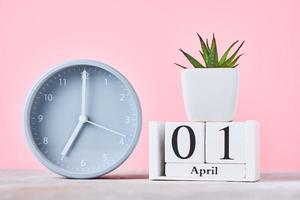 calendario de bloques de madera con fecha 1 de abril, despertador y planta en el fondo rosa foto