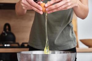 Woman in kitchen cooking a dough. Hands breaks an egg into a bowl photo