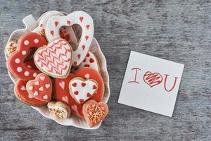 galletas decoradas con forma de corazón y hoja de papel con la inscripción te amo en el fondo gris. concepto del día de san valentín foto