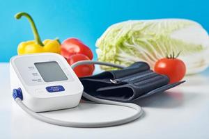 Digital blood pressure monitor and fresh vegetables on the table against blue background. Healthcare concept photo