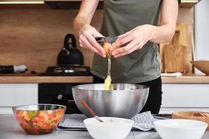 Woman in kitchen cooking a dough. Hands breaks an egg into a bowl photo