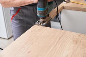 Repairman using electric jigsaw. Sawing place for installing gas hob in worktop photo