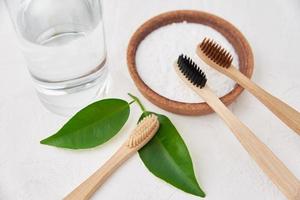 Bamboo toothbrushes, baking soda and glass of water on white background photo