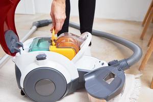 Woman takes out container of dust from vacuum cleaner photo