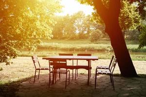 Empty cafe table and chairs under tree in summer day. Ourdoor restaurant photo