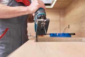 Repairman using electric jigsaw. Sawing place for installing gas hob in worktop photo