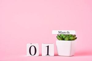 calendario de bloques de madera con fecha 1 de marzo y planta en el fondo rosa. concepto de primavera foto