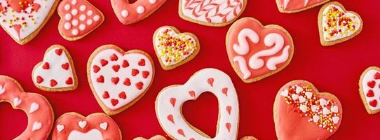 Background of decorated with icing and glazed heart shape cookies on the red background, long banner. Valentines Day food concept photo