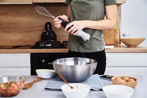 mujer en la cocina cocinando un pastel. manos batir la masa con una batidora eléctrica foto