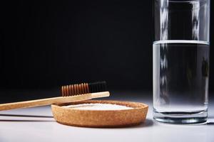 Bamboo toothbrushes, baking soda and glass of water on dark background photo