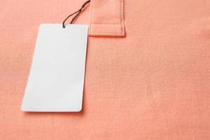 Blank white clothes tag label on pink fabric texture background photo