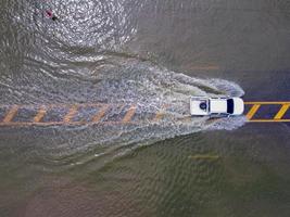 Flooded roads, people with cars running through. Aerial drone photography shows streets flooding and people's cars passing by, splashing water. photo