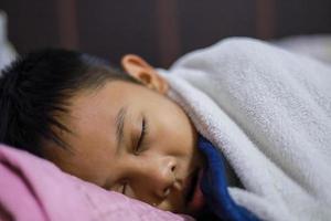 el niño asiático está durmiendo bien en el colchón y la manta en su dormitorio. dulces sueños foto
