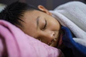 el niño asiático está durmiendo bien en el colchón y la manta en su dormitorio. dulces sueños foto