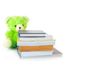 green teddy bear and stack of books on white background photo