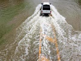 Flooded roads, people with cars running through. Aerial drone photography shows streets flooding and people's cars passing by, splashing water. photo